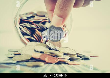 Hand picking up 100 Japanese yen (JPY) coin out of multi currency pile of coins - vintage style color effect Stock Photo