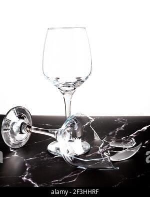 Broken shattered wine glass and shards on marble table against white background. Stock Photo