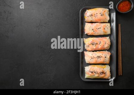 Asian spring rolls with prawn with spicy sauce wrapped in rice paper on black background with copy space. View from above. Stock Photo