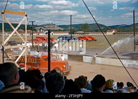 A fire hose demonstration in the arena at the Lycoming County Fair, Hughesville, Pennsylvania, USA c 1955. The powerful jet of water is being aimed at a target. Other emergency response vehicles are in the background. The Lycoming County Fair is an annual event held in the county. This image is from an old American amateur Kodak colour transparency – a vintage 1950s photograph. Stock Photo
