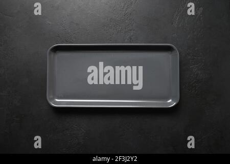 Empty black modern rectangular plate on black background. View from above. Copy space. Kitchen stuff, flat lay for cooking as background. Stock Photo