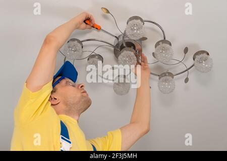 Electrician with glasses screws a chandelier to the ceiling in close-up Stock Photo