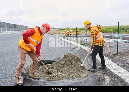 Two construction workers shovel concrete while building a road on a street in the new development area Stock Photo