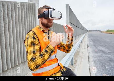 Worker does virtual construction planning with VR glasses on construction site for cyber road construction Stock Photo