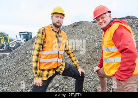 Architect and construction worker stand in front of a mound of earth on the construction site of the house building Stock Photo