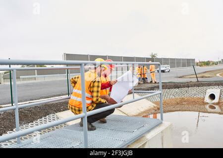 Two construction workers with plan control construction on the road construction site Stock Photo