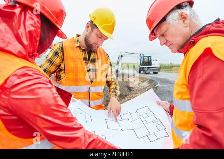 Three construction workers discuss construction plan on the construction site of building a house in the new development area Stock Photo