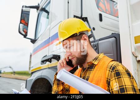 Construction worker calls in front of a truck with mobile phone on the construction site of the road construction Stock Photo