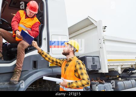 Construction manager with checklist and truck driver discuss delivery at the construction site Stock Photo