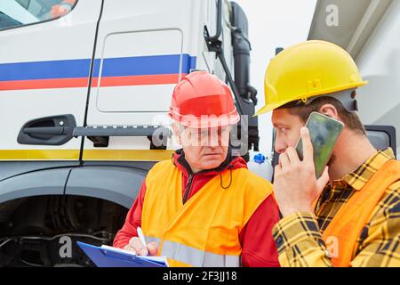 Construction worker and architect with cellphone and checklist in front of truck on a construction site Stock Photo