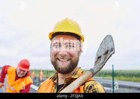 Smiling road builder with hard hat and shovel on road construction site Stock Photo