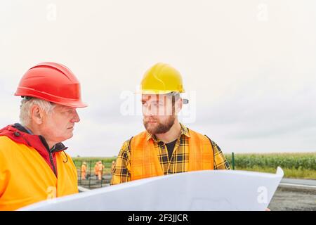 Construction workers and architects plan house or road construction with a blueprint in the new development area Stock Photo