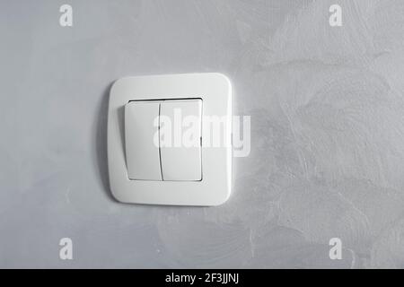 Light switch, a plastic mechanical switch of white color installed on a light gray wall. Stock Photo