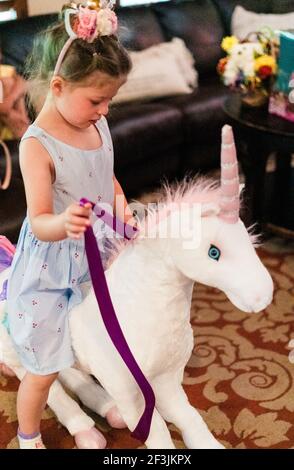 Little girl riding a toy unicorn in the living room. Stock Photo