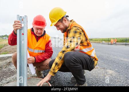 Two construction workers check foundation for guard rails on construction site of road construction Stock Photo