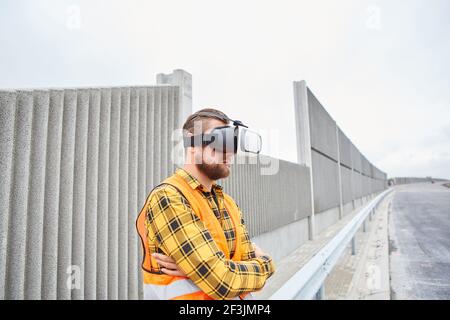 Workers with VR glasses on the road construction site in front of a noise barrier Stock Photo