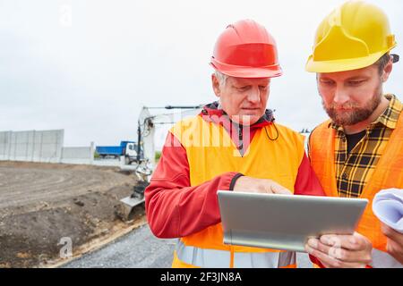 Two workers as a road construction team on a road construction site with excavators Stock Photo
