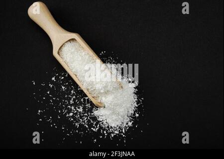 Coconut shavings. Wooden scoop Spoon with Coconut shavings on black background. copy space. Shredded coconut shavings. top view Stock Photo