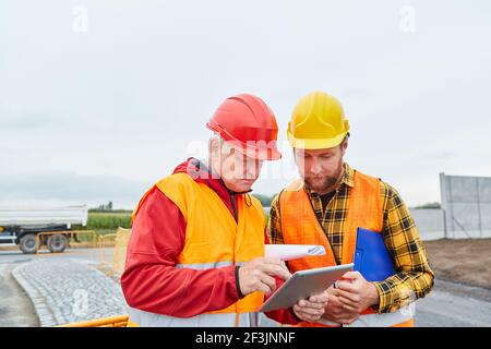 Two construction workers using tablet computer on construction site in road construction or house building Stock Photo