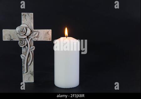 Burning candle on a dark background with an ornate cross. Mourning moment at the end of a life. Last farewell. Copy space. Condolence card. Stock Photo