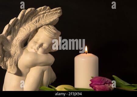 hite angel with candlelight and tulip flowers on a dark background. Moment of grief at the end of a life. Last farewell. Funeral concept. Stock Photo