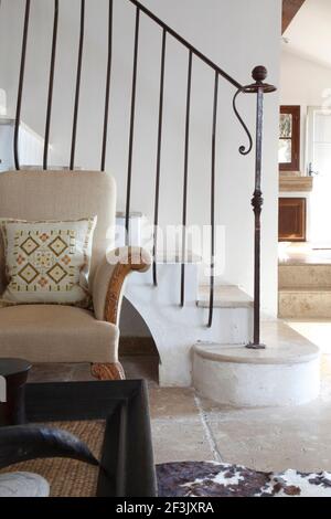 Armchair with carved wooden legs and arms in front of staircase with wrought iron handrail. Glimpse of kitchen beyond, Villa in St Tropez Stock Photo