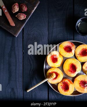 Juicy cut peaches with honey near knife and peach seeds on wooden dark table in the kitchen at country home Stock Photo