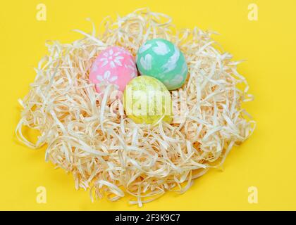 Close up of colored Easter eggs in nest on a yellow background. Hand-painted by a child colored Easter eggs Stock Photo