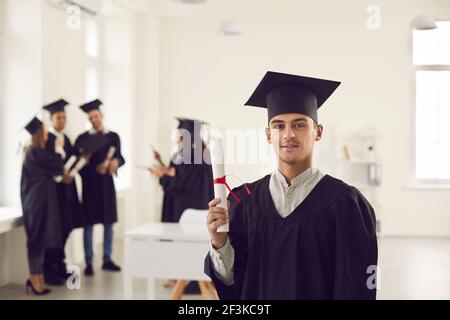 Confident student guy in the uniform of a university graduate showing a diploma in his hands. Stock Photo