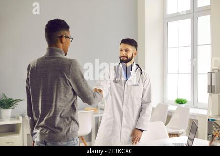 Smiling man doctor therapist shaking hand to black man patient after successful checkup Stock Photo