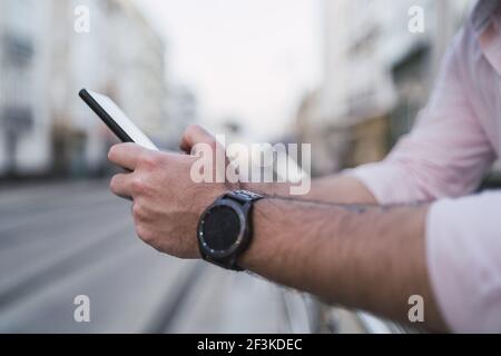 A smartphone in the hands of a male leaning against the street railings and scrolling on the device Stock Photo