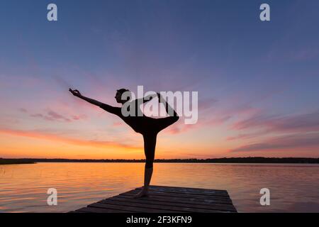 Woman doing yoga exercises on a jetty by a lake, dancer pose. Schleswig-Holstein, Germany Stock Photo