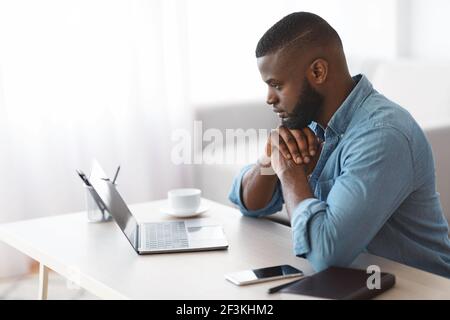 Pensive African American Man Working With Laptop At Home, Side View Stock Photo