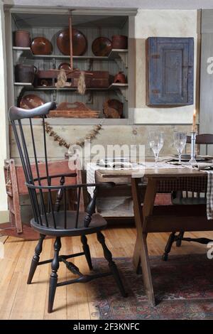 Primitive style dining room with table and chair. In the background a wall cabinet and old plates. Stock Photo
