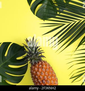 Top view of fresh pineapple with tropical palm and monstera leaves on yellow table background. Stock Photo