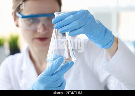 Woman scientist holding flask with transparent liquid in her hands closeup Stock Photo