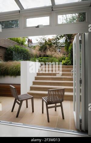 French windows open onto the lower York stone paved outside area, with bench/store and York stone steps leading up to the larger, upper level. Contemp Stock Photo