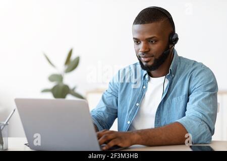 Portrait of african american man in headset working on laptop in office Stock Photo