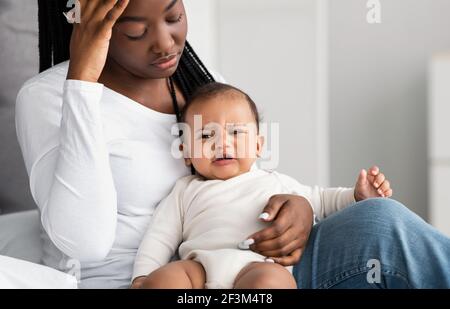 Stressed African American mom sitting with kid on bed Stock Photo