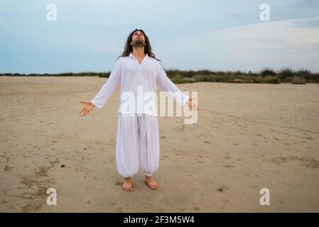 Stock photo of adult man with long hair asking for god in the beach. Stock Photo