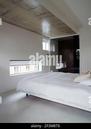 Bedroom with double bed, rectangular and square windows, wooden section of ceiling and mirrored wardrobe door in French residential home. Stock Photo