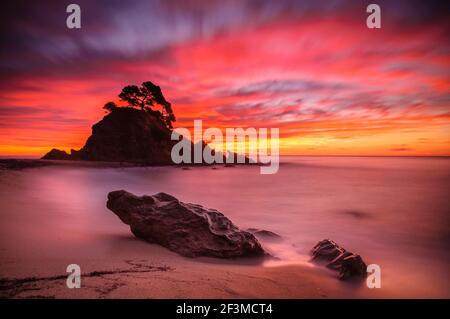 Sunrise with red sky on a mediterranean beach next to an island with pines in Costa Brava (Platja d'Aro, Girona province, Catalonia, Spain) Stock Photo