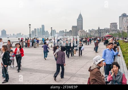 Shanghai, China - May 4, 2010: Many people walk on boardwalk along river Bund side uner silver sky. Skyline as backdrop. Clothing of people adds color Stock Photo