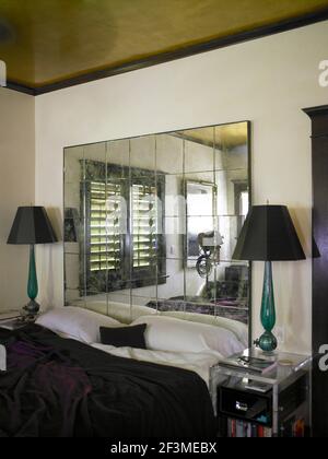 Mirrored tiles on wall behind bed between pair of matching bedside lamps in residential house, California, USA Stock Photo