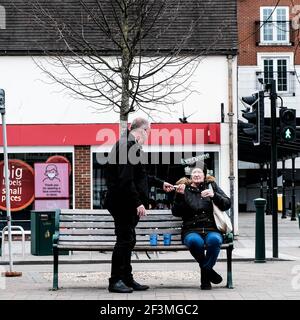 London UK, March 17 2021, Family Couple Sitting Outside On A Wodden Bench Relaxing Having Takeaway Coffee Stock Photo