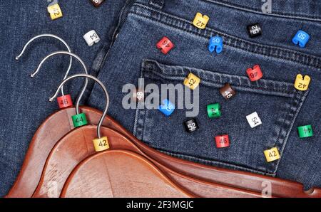 Clothes hangers with multicolored plastic size labels on a denim backdrop. Stock Photo