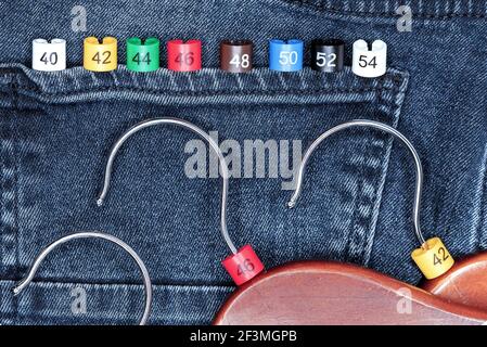 Clothes hangers with multicolored plastic size labels on a denim backdrop. Stock Photo
