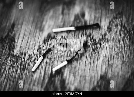 A black-and-white image of three burnt matches lying on a wooden table. One of the matches burned out and broke. Danger. Stock Photo