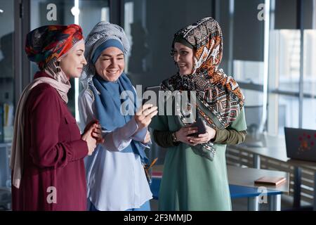 Group of muslim women in hijabs using their mobile phones while standing at office Stock Photo