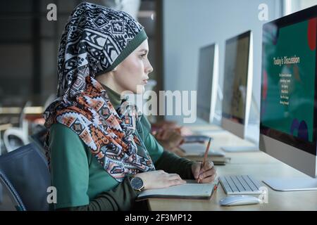 Young muslim businesswoman sitting at the table in front of computer monitor and working on computer at office Stock Photo